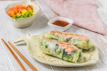 Two summer rolls with salad and salmon and sauce on a white wooden background, japanese, asian food