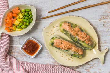 Two summer rolls with salad and salmon and sauce on a white wooden background, japanese, asian food, top view