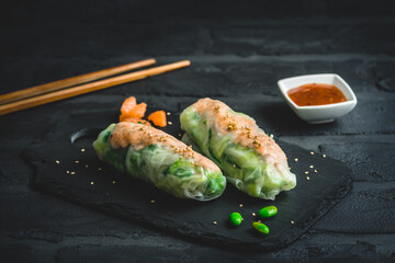 Two summer rolls with salad and salmon on black background, japanese, asian food