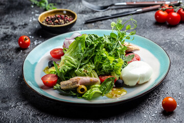 Tuna salad with poached, egg, lettuce, cherry, tomatoes olives and corn on dark stone or concrete background. Top view. copy space