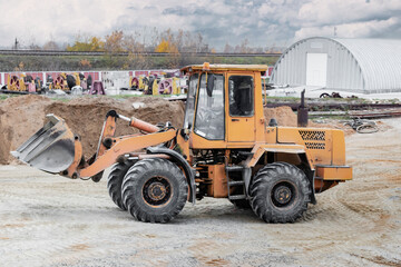 The loader is transporting sand or gravel in the front bucket. Heavy construction equipment at a construction site. Transportation of bulk materials in a concrete plant.