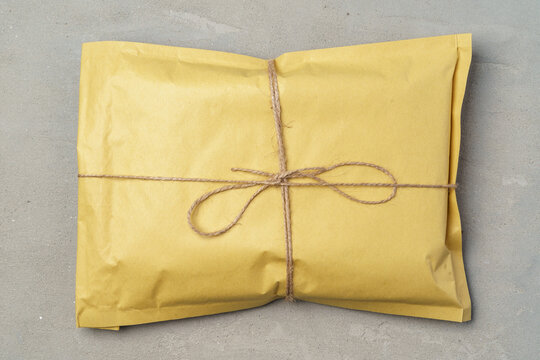 Yellow paper parcel post tied with twine on gray background top view