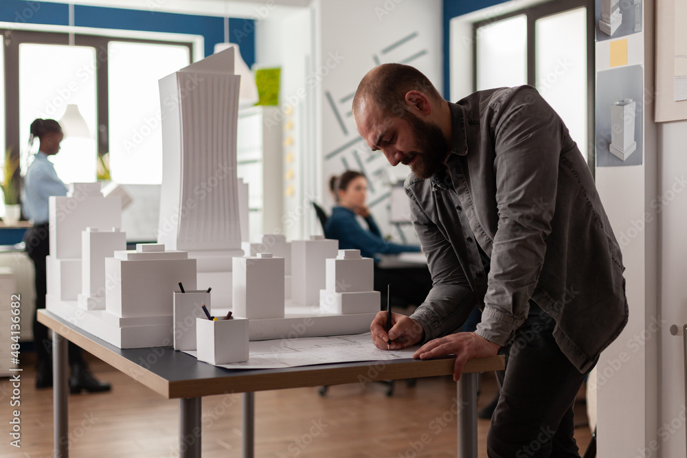 Aufkleber architect drawing blueprints at desk in modern architectural office next to white foam scale model o