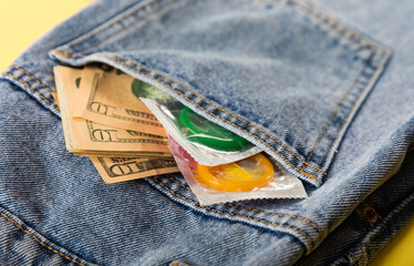 condoms and money in jeans on a yellow background. The concept of safe sex, prevention of sexually transmitted diseases.