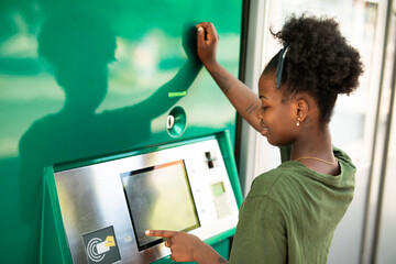 Beautiful African girl using ATM machine. Happy smiling young woman withdrawing money from credit card