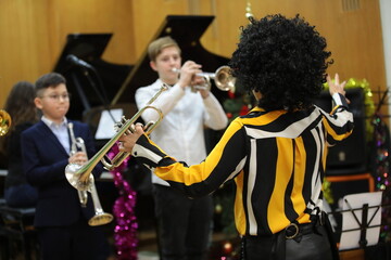 A female musician with a musical instrument in her hand a trumpet leads a school orchestra jazz band celebratory performance with children