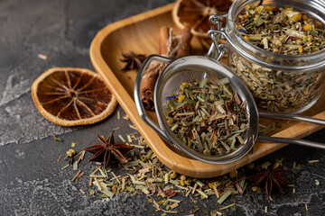 Herbal tea with green tea leaves in a transparent jar, tea in a strainer on a wooden plate and on a...