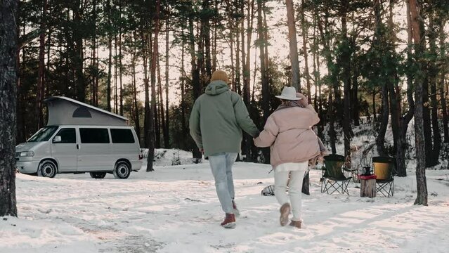 Romantic couple happily walk through wood camp holding hands, enjoying van life. Couple of tourists living in a van with pop-up roof. Campers stopping at the woods. High quality 4k footage
