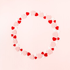 Round frame made of little red and white wooden hearts on pink background