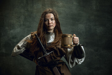Portrait of medieval female warrior or knight with dirty wounded face holding huge mug of beer...
