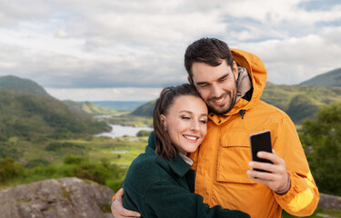 technology, travel and travel concept - happy couple with smartphone over river valley at Killarney...