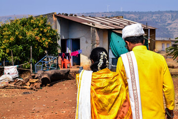 Fototapeta premium Back view of newly married Indian couple, bride wearing yellow color saree ,groom wearing yellow color kurta and white color cap. Both are walking toward their home