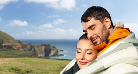 travel, tourism and love concept - happy smiling couple in warm blanket over big sur coast in california background
