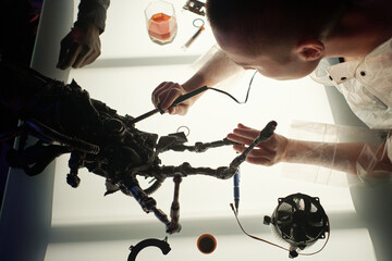 Hands of young female cyberpunk with electric instrument repairing electronic equipment while...