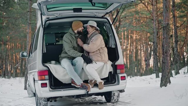 Romantic couple sitting at the back of van in the woods on a sunny winter day. Couple of tourists living in a van with pop-up roof. Campers having a stop at the woods. High quality 4k footage