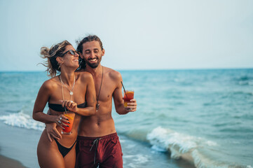 Attractive young couple with alcohol cocktails walking on the beach
