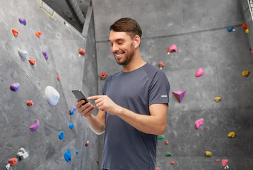 fitness, sport and bouldering concept - smiling man in sports clothes with smartphone and earphones listening to music over climbing wall at gym on background © Syda Productions