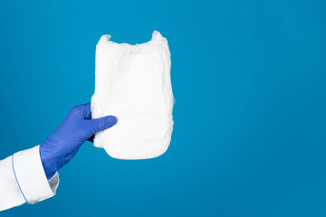 Doctors hand in a glove holds a baby diaper pant on a blue background with copy space