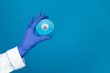 Doctors hand in a glove holds a kinesiology tape on a blue background with copy space