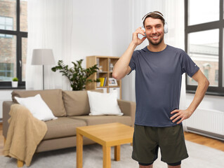 fitness, sport and healthy lifestyle concept - smiling man in sports clothes with headphones listening to music over home room background