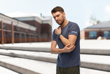fitness, sport and healthy lifestyle concept - man with smart watch or tracker holding to injured hand over city street background
