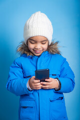 Asian youth smiling as she reads message on her smart phone, wearing winter clothes and blue background. concept of addiction to smart phones.