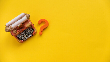 Questions and answers concept. Question symbol and miniature typewriter on yellow background with copy space.