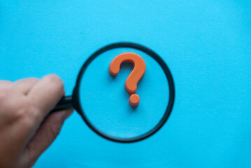 Questions and answers concept. Question symbol and hand holding magnifying glass on blue background.