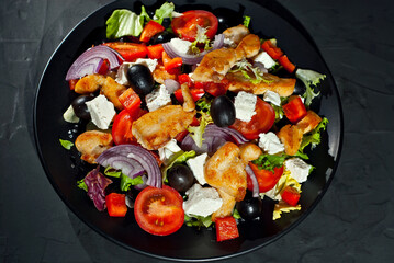 Salad with tomatoes, peppers, olives and chicken fillet. Fresh salad in a black plate on a dark background.