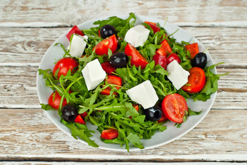 Greek salad in a white bowl. Fresh vegetable salad on a white background. Food on a shabby table. Bowl on an old wooden board.