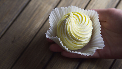 Meringue in hand on wooden background, close up. Food harmful to diabetics.