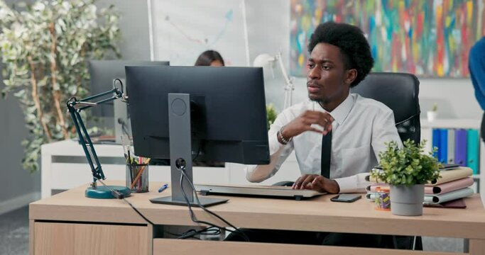 An experienced handsome company employee dressed in a shirt and tie prepares documents on the computer, drafts an article or a speech, sends messages to clients, taps fingers on the keyboard