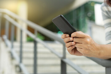 Young woman wear a dress using modern smartphone device typing text message in social media while sitting on stairs outdoor. Happy female spending free time in break of working.