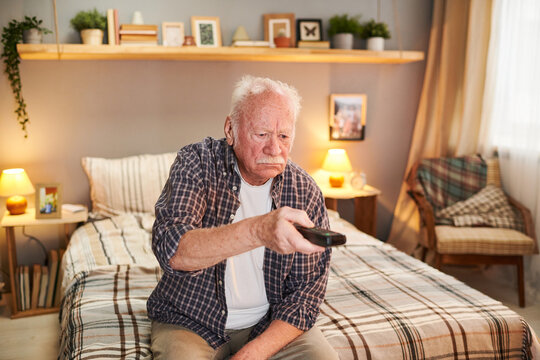 Old Man With White Hair Sitting On The Bed And Watching TV During His Leisure Time At Home