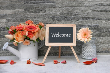 Chalk board with the word welcome with roses and gerberas in a vase