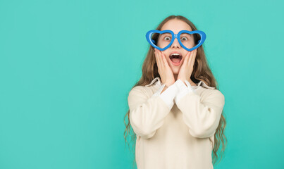 surprised teen girl in party glasses on blue background with copy space, fancy