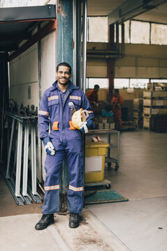 Portrait of smiling male blue-collar worker in protective workwear at entrance of factory