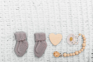 Gray knitted baby socks, a pacifier and a heart on a blue soft blanket. Child expectation concept. Cute things for a newborn. Copy space, flat lay, top view.
