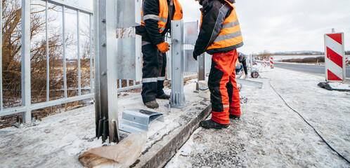 Road workers installing a new fence railing of bridge, outside the city 