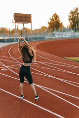 Woman in sportswear with perm curly hair is stretching on a stadium in the morning.