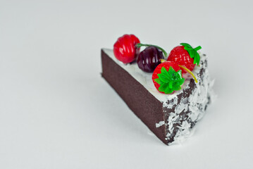 A piece of brown cake on a white background. Cake with strawberries and cherries close up.