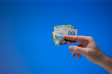 Swiss franc banknotes held by male hand. Close up studio shot, isolated on blue background