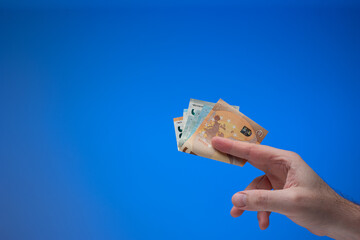 Euro currency banknotes held by male hand. Close up studio shot, isolated on blue background - obrazy, fototapety, plakaty