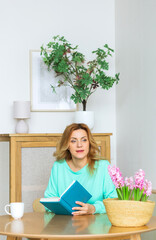 Beautiful woman in green pajamas sits at the kitchen table with a notebook in her hands.