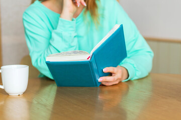 Obraz premium Mature woman drinking tea from cup and writing down thoughts or ideas in notebook and planning her day while standing behind kitchen table at home in morning