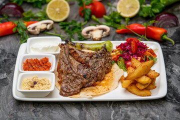 Grilled lamb chops with french fries and appetizers on a white porcelain plate