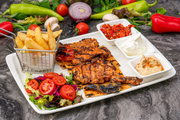 Grilled chicken thigh on white porcelain plate with french fries and salad