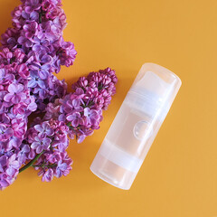 Transparent bottle of intimate lubrication gel and pink lilac flowers on yellow background. Water...