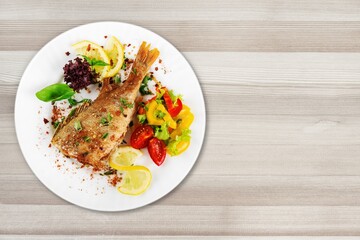 Plate of fried fish fillet with vegetables on the desk
