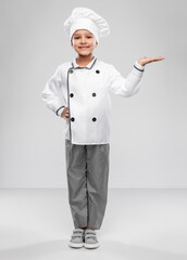 cooking, culinary and profession concept - happy smiling little girl in chef's toque and jacket holding something imaginary on hand over grey background